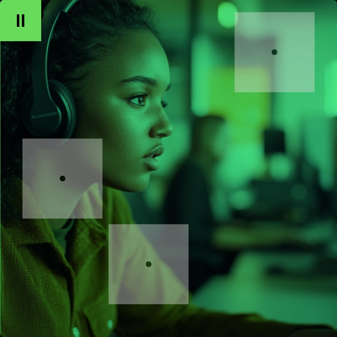 A young woman wearing headphones, focused on a computer screen in a green-lit room.