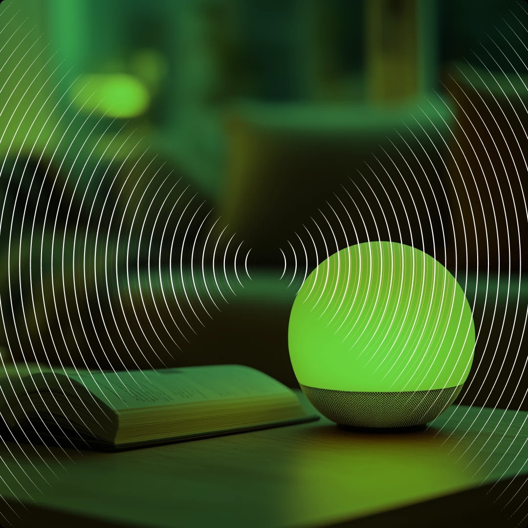 A smart speaker emitting a green glow, placed on a table next to an open book, with a blurred background and white concentric circle design overlay.