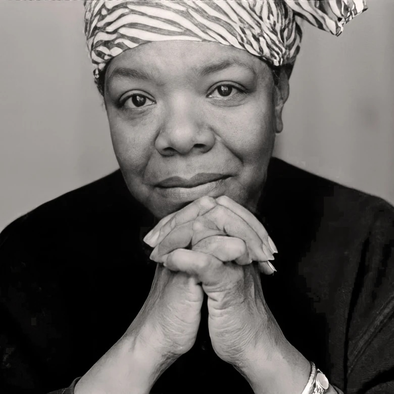 A woman wearing a headscarf, resting her chin on her clasped hands, looking directly at the camera.