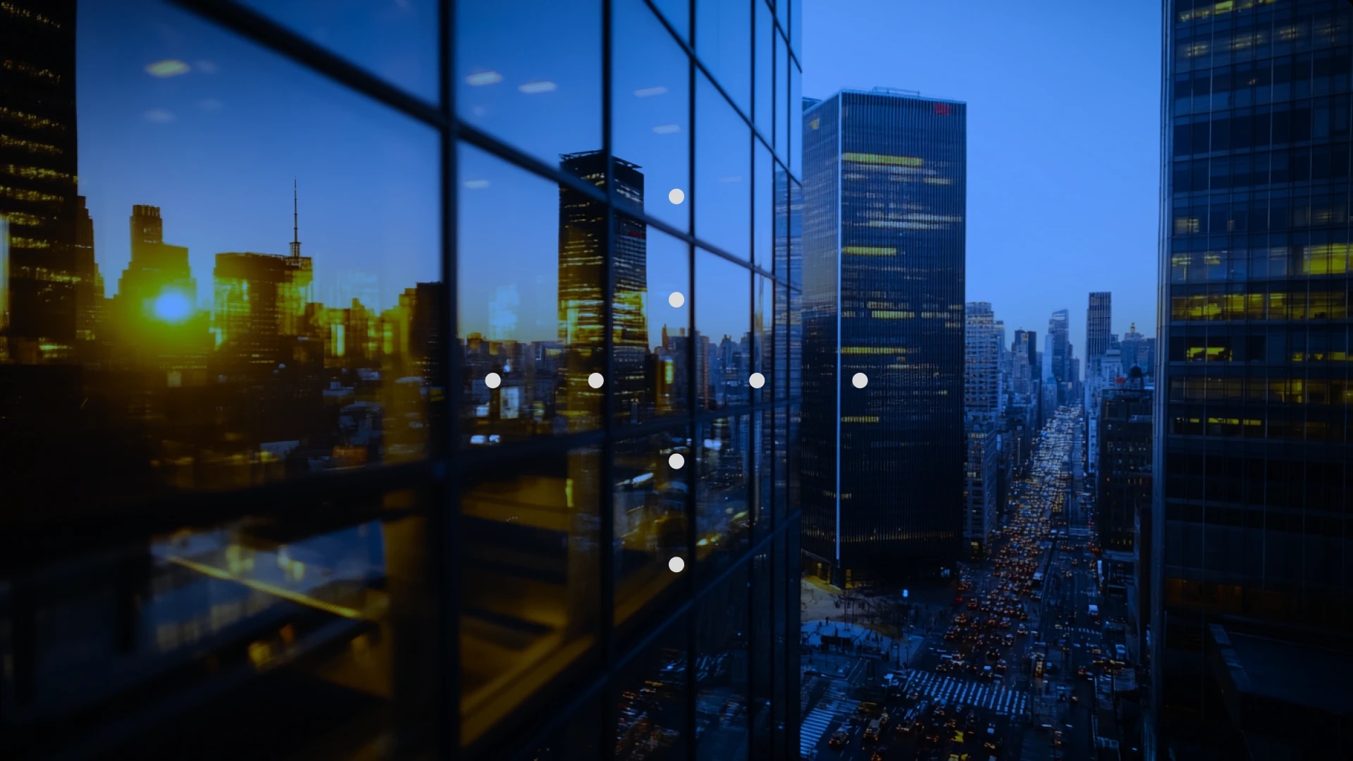 Cityscape at dusk with tall glass buildings reflecting the evening sky and city lights.